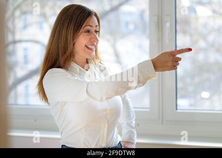 Femme professionnelle pointant de côté avec une expression sérieuse et intense focalisée regardez comme elle se tient devant une grande fenêtre Banque D'Images