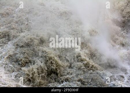 L'eau qui fait rage dans une rivière de montagne boueuse après une chute d'eau Banque D'Images