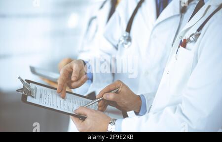 Des médecins inconnus, deux hommes et une femme, discutent des examens médicaux, tout en se tenant au bureau de l'hôpital. Médecins utilisant des planches à découper pour remplir Banque D'Images