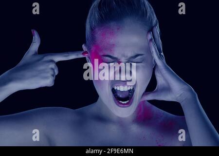 Femme en maquillage artistique sur fond sombre, tenant le doigt sur le temple, simulant un cliché Banque D'Images