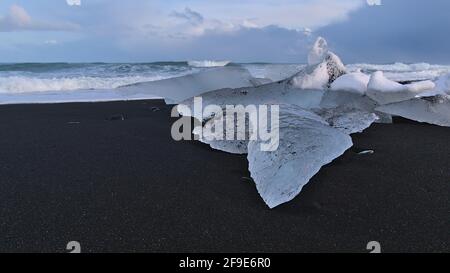 Petit iceberg avec des formations de glace bizarres sur la plage de diamants près de Jökulsárlón et périphérique dans le sud de l'Islande en soirée lumière du soleil avec la mer agitée. Banque D'Images