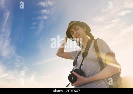 fille touriste avec un sac à dos et un appareil photo sur le fond du ciel bleu et du coucher du soleil, des photos de bas en haut. Banque D'Images