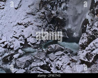 Vue rapprochée en grand angle du fond de la cascade Hundafoss dans le parc national de Skaftfaell, dans le sud de l'Islande, en hiver, avec des rochers gelés en cours d'eau. Banque D'Images