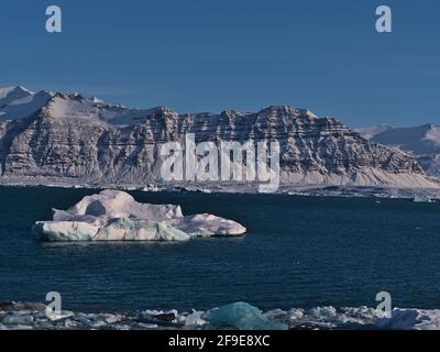 Vue imprenable sur le glacier lagon Jökulsárlón, situé dans le parc national de Vatnajökull dans le sud de l'Islande, avec un grand iceberg flottant et des montagnes accidentées. Banque D'Images