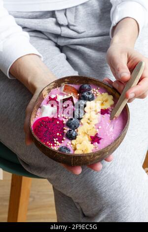 Angle de récolte élevé femelle méconnaissable avec bol motorisé plein de tranches de banane fraîche et de pitaya avec smoothie et bleuets Banque D'Images