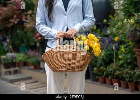 fille tenant un panier en osier avec des fleurs jaunes, elle est en face d'un magasin de fleurs. Banque D'Images