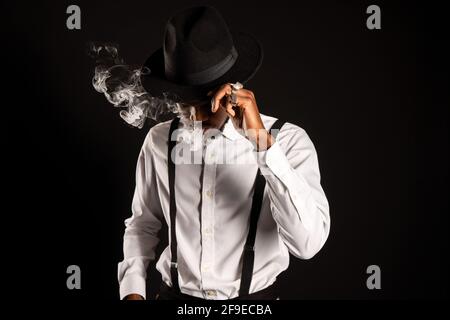 Masculin afro-américain en chemise blanche et chapeau exhaling vapeur tout en fumant e cigarette Banque D'Images