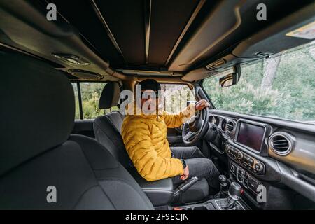 Vue intérieure d'un conducteur portant une casquette et des lunettes de soleil dans une voiture tout-terrain regardant la caméra Banque D'Images