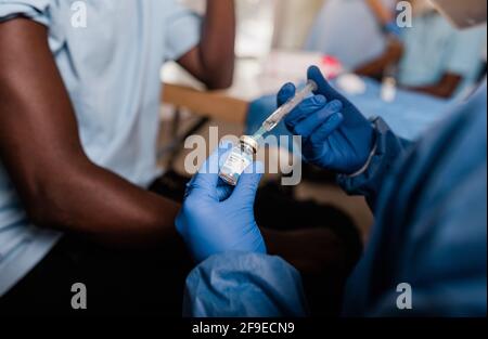 Crop mains de médecin anonyme en latex gants de remplissage seringue du flacon contenant le vaccin se préparant à vacciner un mâle méconnaissable Afro-américain Banque D'Images