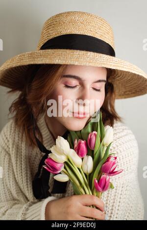 Femme rêveuse en robe et avec des fleurs de tulipe délicates debout avec des yeux fermés sur fond blanc en studio Banque D'Images