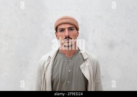 Homme sérieux portant un manteau et un chapeau tendance debout en ville et regarder l'appareil photo Banque D'Images