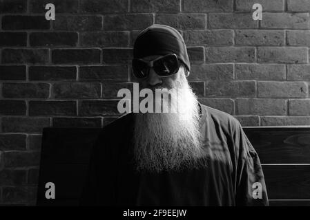 Portrait noir et blanc de l'homme mûr avec un long gris barbe portant un bonnet et des lunettes de soleil Banque D'Images