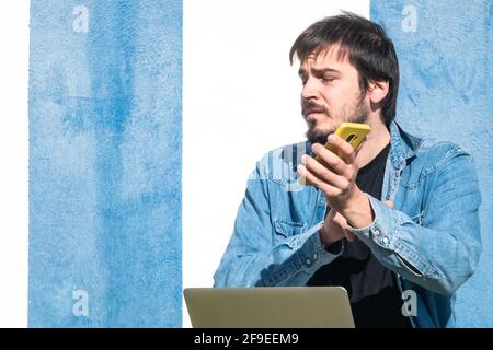 Un homme espagnol avec un ordinateur portable sur ses genoux et tenir un phonbe mobile tout en étant assis sur l'herbe Banque D'Images