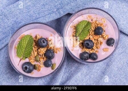 Vue de dessus de deux verres de yaourt à la fraise avec bleuets et des céréales sur une nappe bleue Banque D'Images