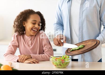 Joyeux père afro et fille cuisant la salade ensemble Banque D'Images