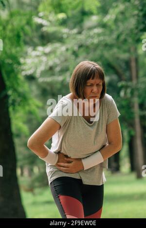 Jogging féminin avec grimace douloureux de visage après avoir ressenti la douleur dans abaisser l'abdomen pendant la course en position de stationnement Banque D'Images