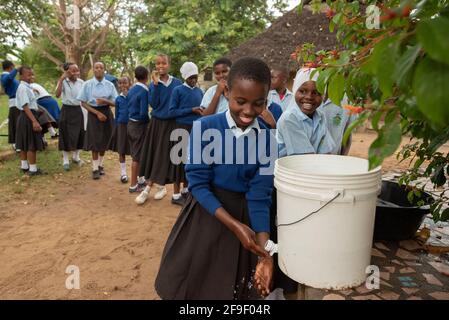 Dodoma, Tanzanie. 08-18-2019. Une fille africaine souriante se lave les mains après avoir déjeuné à l'école tandis que d'autres élèves attendent dans la file d'attente. Banque D'Images