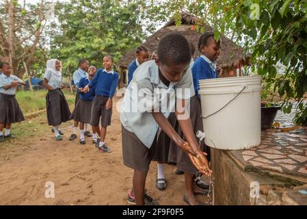 Dodoma, Tanzanie. 08-18-2019. Un garçon africain se lave les mains tandis que d'autres étudiants s'amusent en attendant dans la file pour leur tour. Banque D'Images