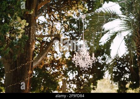 Un lustre en cristal et une guirlande sont suspendus d'un arbre. Décorations de mariage pour le banquet à l'extérieur. Banque D'Images