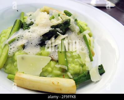 Mousse fraîche formée sur risotto une cuisine italienne avec asperges, noix et morceaux de fromage sur plaque blanche. Mise au point sélective extrême Banque D'Images