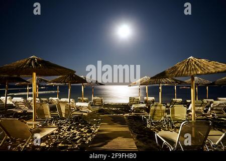 Videz les chaises longues et les parasols sur la plage de sable sous la lune la nuit sur l'île de Zakynthos, en Grèce Banque D'Images