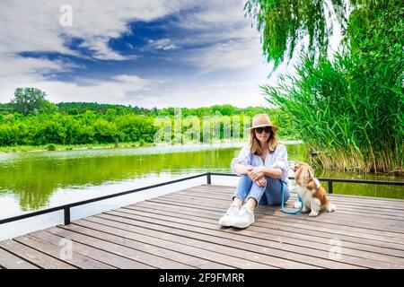 Prise de vue en longueur d'une femme assise à côté de son mignon petit chiot de cavalier sur la jetée tout en se relaxant au lac. Banque D'Images