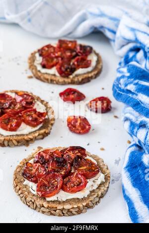 Tranches rondes de pain complet avec tomates grillées et herbes sur fromage à la crème. Gros plan vertical. Banque D'Images