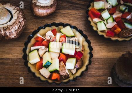 Gros plan de tartelettes de légumes crus dans des plats à tarte noirs sur une table en bois, préparés pour la cuisson. Banque D'Images