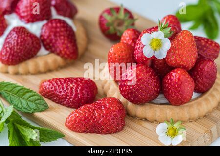 Tartelettes aux fraises en bois, décorées de fleurs, de fraises et de feuilles de menthe. Gros plan. Banque D'Images