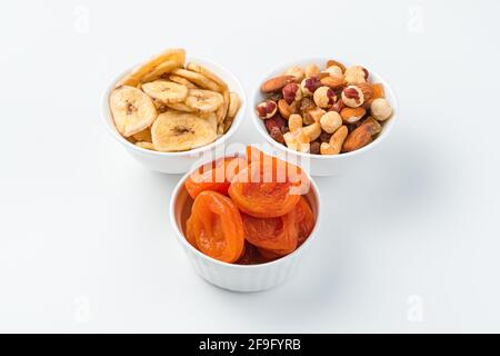 Abricots séchés, chips de banane et un mélange de noix dans trois bols sur fond blanc. Des collations saines. Banque D'Images