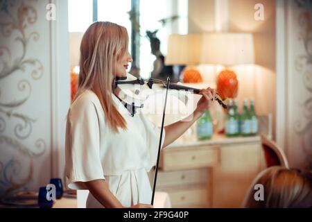 une fille blonde dans un ensemble blanc joue le violon blanc dans un restaurant Banque D'Images