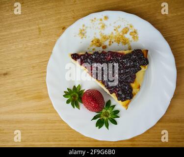 Tranche de cheesecake avec une fraise et garnie d'un biscuit émietté. Gâteau au fromage dans un plat blanc. Vue de dessus Banque D'Images