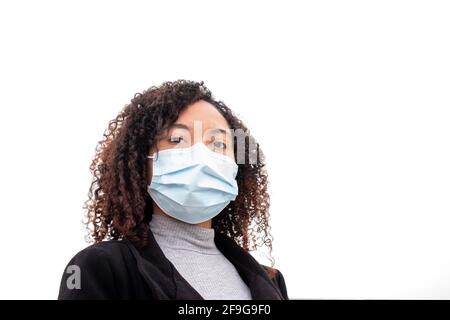 Belle jeune femme à la peau sombre avec des cheveux bouclés portant un masque de protection contre le virus COVID regarde avec confiance l'appareil photo. Banque D'Images