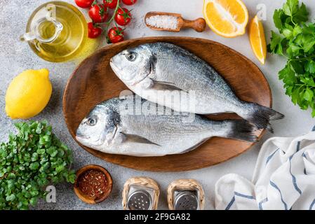 Poisson dorado non cuit sur un plateau en bois avec un cadre de légumes et d'épices et de l'huile d'olive prêt à cuire, vue sur la table. Processus de repas de cuisine, med Banque D'Images