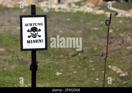 Un signe de crâne avec l'inscription attention mines en allemand 'Achtung minen' à la clôture de la zone de danger avec barbelés près du champ de mines, personne. Banque D'Images