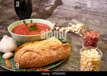 Gazpacho dans un bol avec persil. Accompagné de pain et d'ail, et sur la droite, il y a des croûtons, du jambon Serrano et des œufs. À l'arrière l'ombre de l'olive Banque D'Images