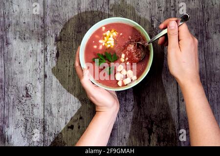 Zénith vue d'un bol de gazpacho avec garniture d'accompagnement, étant tenu par des mains humaines, prêt à déguster avec une cuillère. Avec ombre. Concept de méditerranée Banque D'Images