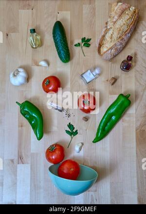 Les ingrédients andalous de gazpacho quittent le bol et s'étendent à travers la table. Il y a des tomates, des poivrons, de l'ail, du concombre, du persil, pain,. Banque D'Images