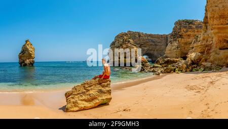 Jeune homme assis sur un rocher, plage de Praia da Marinha, côte rocheuse, formation rocheuse dans la mer, Algarve, Lagos, Portuga Banque D'Images