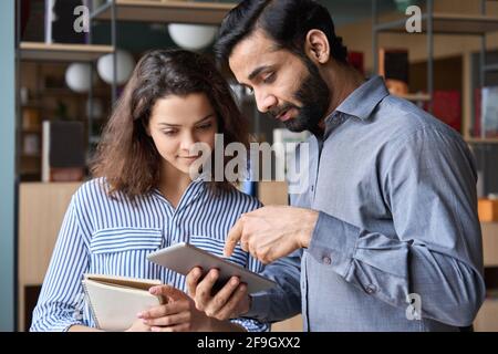 Un responsable indien et un jeune employé latin qui parle au bureau à l'aide d'une tablette. Banque D'Images