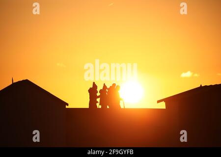 Heacham, Royaume-Uni. 14 avril 2021. Les gens, silhouetés contre le ciel orange au coucher du soleil, marchant derrière le mur de la promenade et des cabanes de plage à Heacham, Norfolk. Crédit : Paul Marriott/Alay Live News Banque D'Images