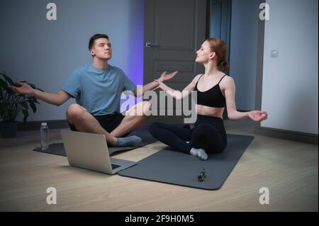 La maison des jeunes mariés pour les cours de yoga, ils méditent sur le sol sous une vidéo avec de la musique relaxante à partir d'un ordinateur portable. Banque D'Images