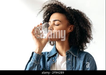 Un mode de vie sain. La jeune femme afro-américaine boit avec plaisir un verre d'eau pure. Belle femme en bonne santé suivre un mode de vie sain, se soucie de la santé Banque D'Images