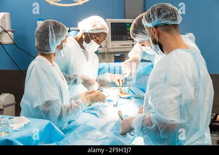 Une équipe internationale de médecins effectue une opération chirurgicale complexe sur un patient sous anesthésie. Salle d'opération moderne et chirurgiens expérimentés Banque D'Images