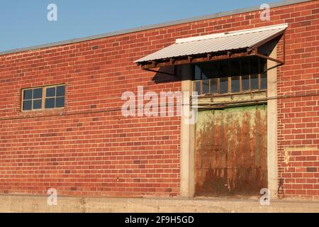 La peinture s'estompe sur une porte de quai de chargement d'un bâtiment abandonné en brique rouge. Banque D'Images
