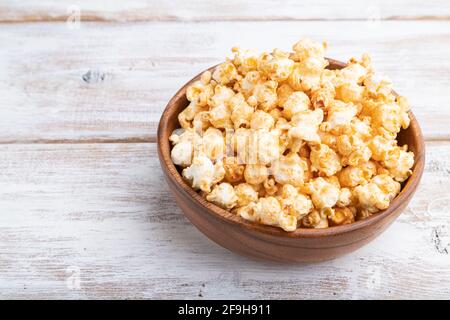 Pop-corn au caramel dans un bol en bois sur fond de bois blanc. Vue latérale, gros plan. Banque D'Images