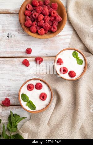 Yaourt à la framboise dans des tasses en argile sur fond de bois blanc et linge textile. Vue de dessus, plat, gros plan. Banque D'Images