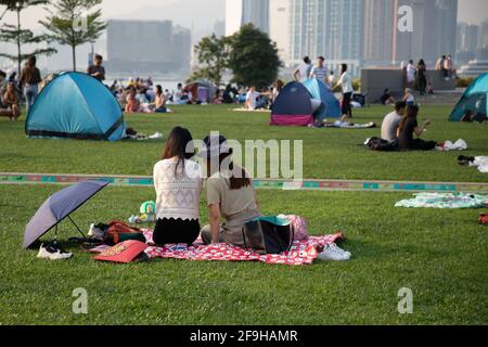 20 3 2021: Deux femmes chinoises , amis familles assis et se reposant sur le terrain d'herbe à Tamar Park, Hong Kong pendant Covid-19, avec beaucoup d'autres similaires Banque D'Images