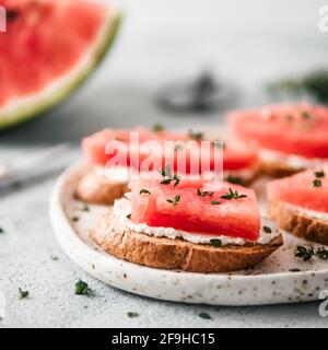 Toasts avec du fromage à pâte molle, de la pastèque et thym frais.salé sucré,fromage pastèque et épicé sur croquant de thym pain grillé tranches. Idée et recette pour un petit-déjeuner sain, inhabituelle en goûter d'été Banque D'Images