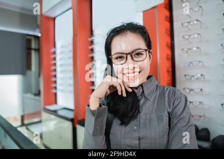 une belle femme souriante portant des lunettes contre le fond de un présentoir à lunettes Banque D'Images